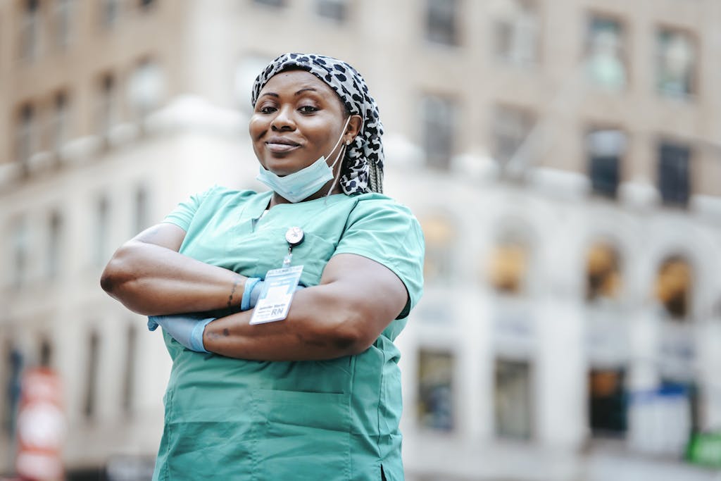 Proud nurse with arms crossed, in uniform, outdoors, urban setting, showing confidence and professionalism.